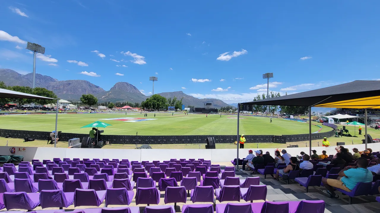 Boland Park cricket field, purple spectator seats and mountains beneath a blue sky.