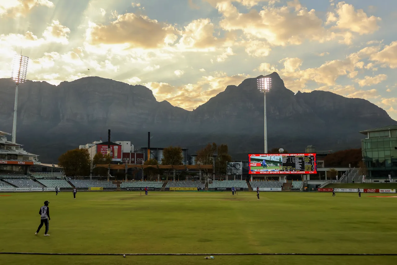 Cricket at Newlands beneath floodlights, mountains and a golden evening sky.
